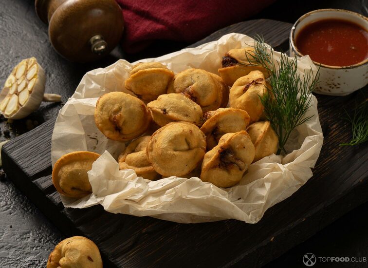 2021-09-08-a4crfe-roasted-homemade-dumplings-with-meat-dill-ketchup-garlic-and-bay-leaf-near-a-pepper-shaker-and-napkin-on-a-black-table