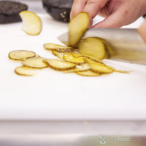 нарезает маринованные огурцы