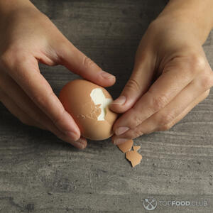 чистит куриное яйцо