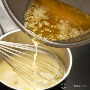 Как только желтки станут кремообразными и плотными, начните медленно добавлять растопленное сливочное масло