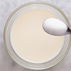 В большую миску влейте теплое молоко, добавьте сахар 